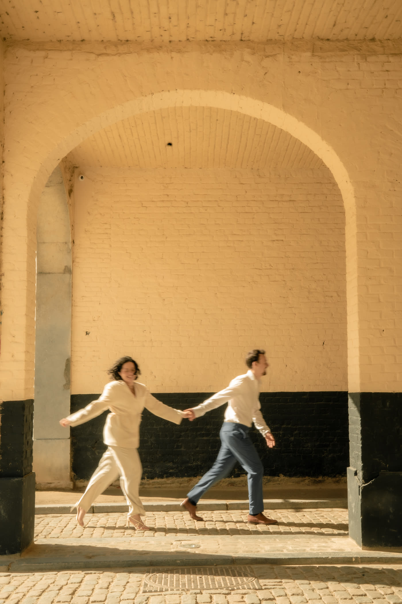 Simon et Laura courant main dans la main sous une arche de briques, photo en mouvement