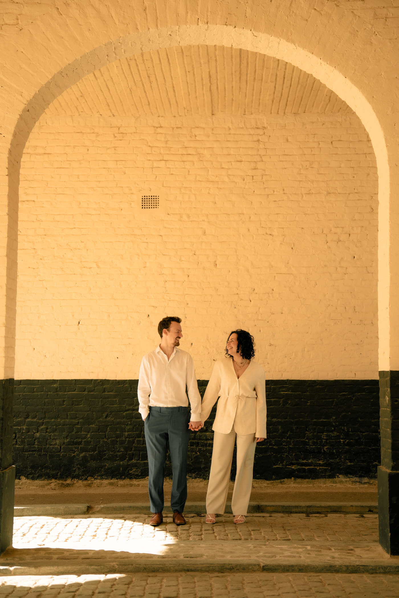 Simon et Laura main dans la main sous une grande arche de briques claires